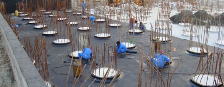Crew waterproofing multiple pile heads across a raft slab