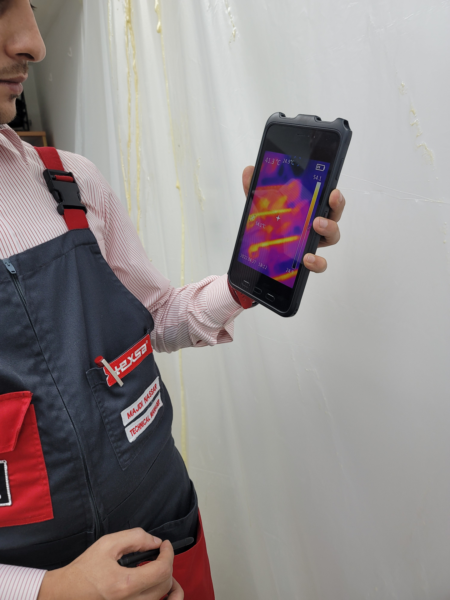 TEXSA technical manager holding a thermal imaging camera against a leaking wall, showing a hot spot revealing the moisture path behind the finish